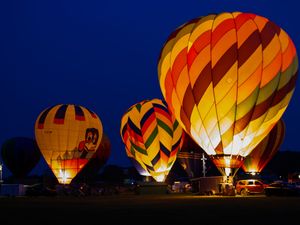Colorful hot air balloons glowing vibrantly against a dark blue night sky at an outdoor balloon festival.