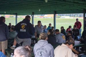 Group of people gathered under a green pavilion at an outdoor sports field event.