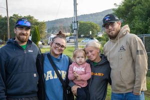 Group of five people including a toddler posing outdoors near a grassy area with mountains in the background.