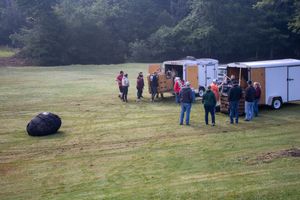 Group of people gathering near trailers on a green field, with a large deflated hot air balloon on the grass.