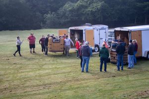 Group of people gathered in a green field near trailers and equipment during an outdoor hot air balloon event.