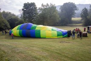 Colorful hot air balloon being inflated on green grass field with crew members and trees in background.