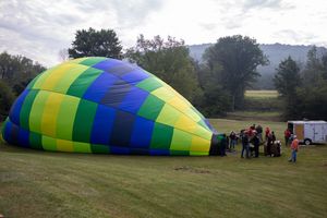 Colorful blue, green, and yellow hot air balloon being inflated on a grassy field with crew members nearby.