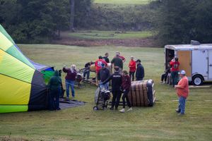 Group of people preparing a hot air balloon for launch in a green field, with colorful balloon envelope visible.