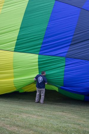 Man standing beside a large colorful hot air balloon being inflated on green grass, featuring blue, green, and yellow stripes.