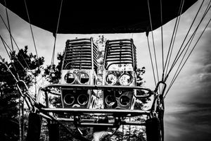 Black and white close-up of a hot air balloon burner and basket rigging against a cloudy sky.