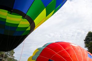 Colorful hot air balloons inflating on the ground against a cloudy sky, showcasing vibrant rainbow stripes and red dome.
