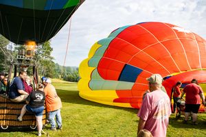 Colorful hot air balloons being inflated on green grass at an outdoor balloon festival with spectators watching.