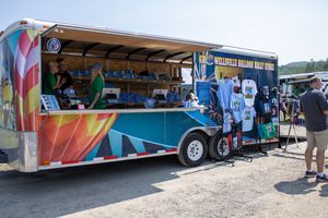 Colorful branded merchandise trailer with t-shirts on display at an outdoor event on a sunny day.