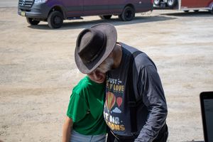 Two people sharing a warm embrace outdoors, one wearing a brown fedora hat and gray jacket, the other in a green shirt.