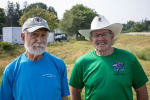 Two smiling men outdoors, one in a blue cap and shirt, other in a white cowboy hat and green shirt.