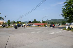 Busy small-town intersection with pedestrians, parked cars, and commercial buildings under a clear blue sky.