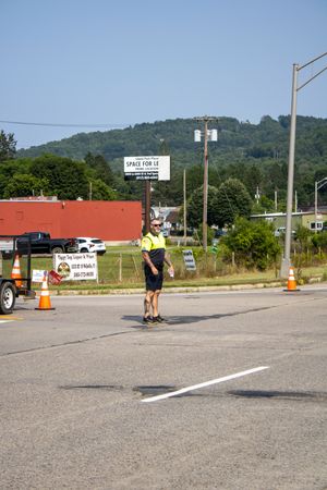Traffic control worker in yellow vest directing vehicles at a road construction zone with orange cones on a sunny day.