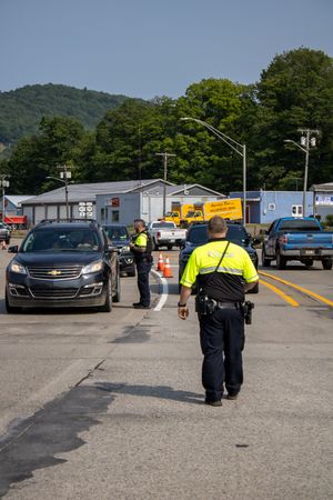 Police officers in high-visibility vests direct traffic at a busy road checkpoint with vehicles queued on a sunny day.
