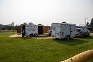 Outdoor event setup with white trailers on green grass, including a Endless Memories trailer, on a hazy day.