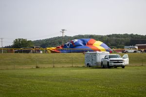 Colorful hot air balloon being inflated on a green field with a white truck and trailer nearby.