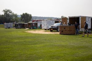 Food trucks and vendor trailers lined up on a grassy field at an outdoor event on a sunny day.