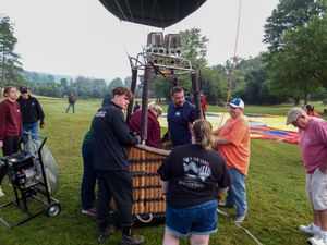 Group of people preparing a hot air balloon for launch on a green field, working together around the basket.