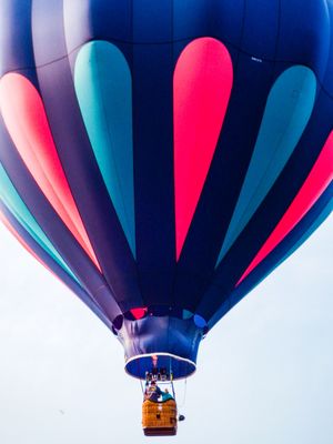 Colorful hot air balloon with pink, teal, and blue panels soaring against a clear sky with passengers in the basket.