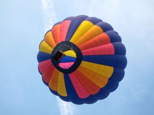 Colorful hot air balloon viewed from below against a blue sky, featuring red, yellow, blue, and pink panels.