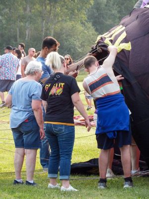 Group of people working together to inflate a large hot air balloon on a grassy field outdoors.