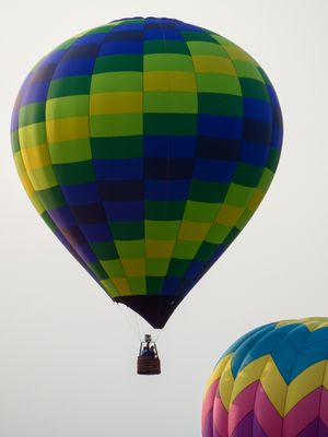 Colorful checkered hot air balloon in blue, green, and yellow floats against a gray sky at a balloon festival.