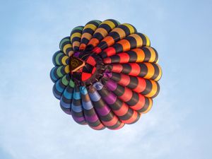 Colorful hot air balloon viewed from below against a blue sky, displaying vibrant rainbow pattern segments.