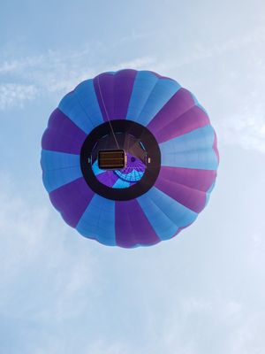 View from below of a purple and blue hot air balloon floating against a cloudy sky.