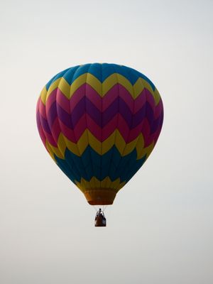 Colorful chevron-patterned hot air balloon with teal, purple, pink, and yellow stripes floating against a gray sky.