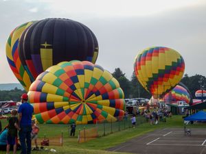 Colorful hot air balloons inflating on a grassy field at a balloon festival with spectators watching nearby.