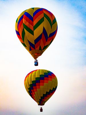 Two colorful hot air balloons with chevron patterns float against a pastel sky during a balloon festival.