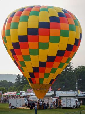 Colorful checkered hot air balloon in yellow, red, green, and blue rising above a crowd at an outdoor festival.