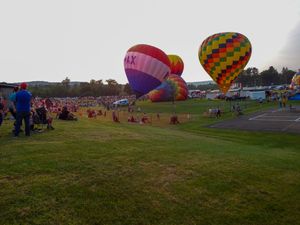 Hot air balloons inflating at a colorful outdoor festival on a green field with a large crowd of spectators gathered nearby.