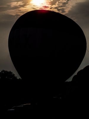 Silhouette of a hot air balloon against a dramatic sunset sky with glowing red sun and clouds.