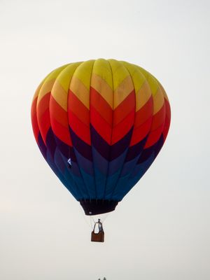 Colorful hot air balloon with rainbow chevron pattern soaring high in a clear sky with passengers in the basket below.