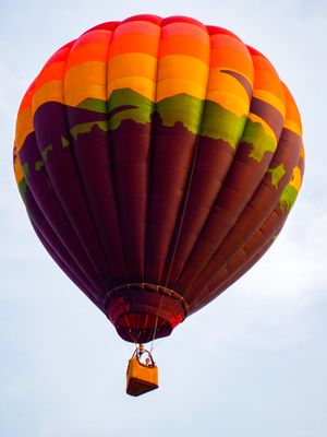 Colorful hot air balloon with rainbow stripes soaring against a clear sky.