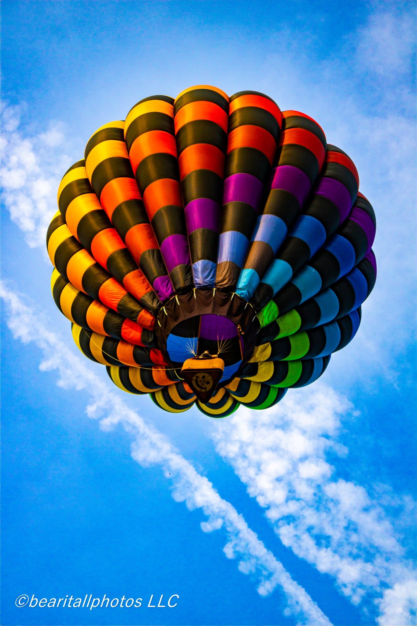 Colorful hot air balloon with rainbow stripes soaring against a bright blue sky with wispy clouds below.