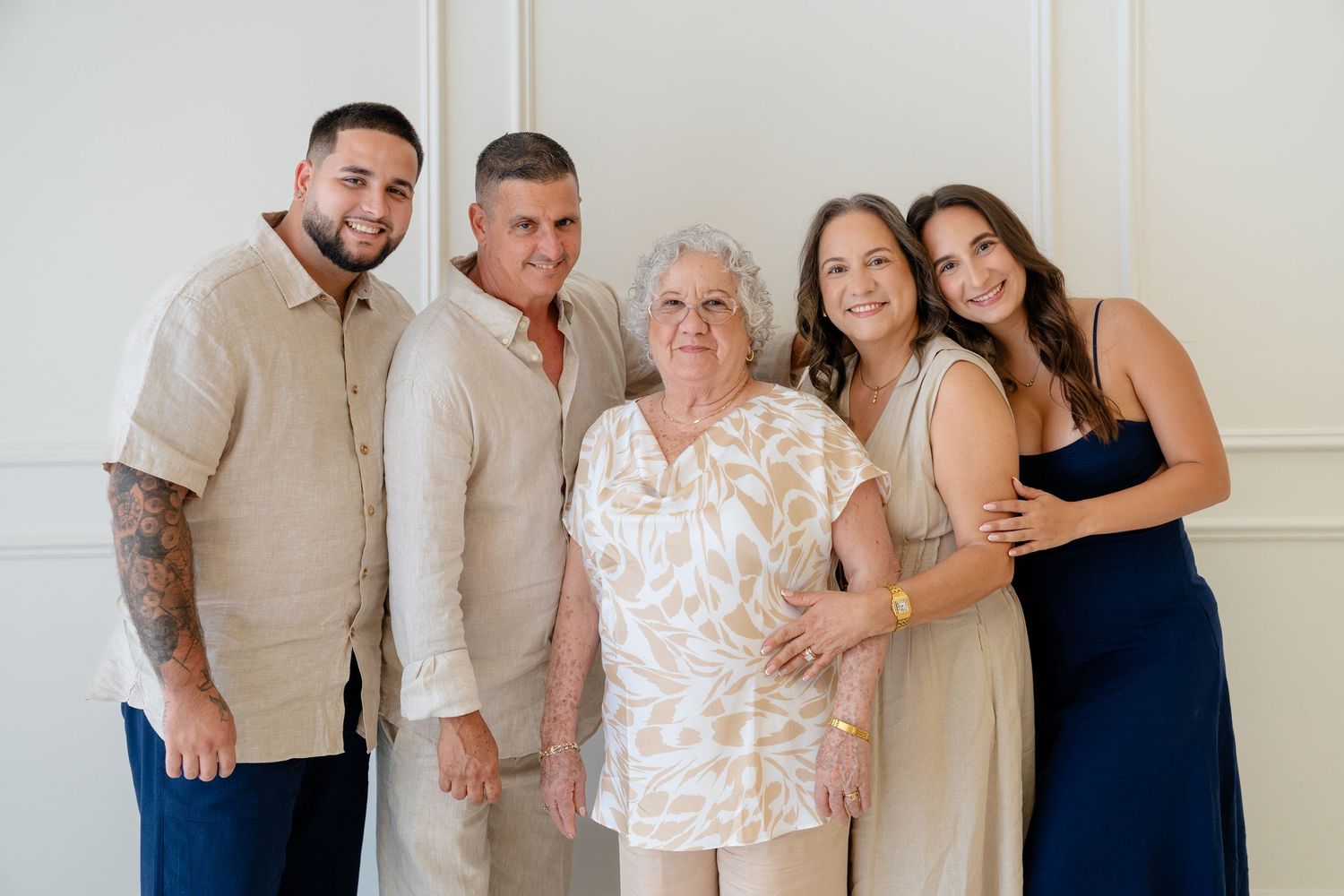Family of five smiling together in elegant attire, posing for a portrait against a white wall.