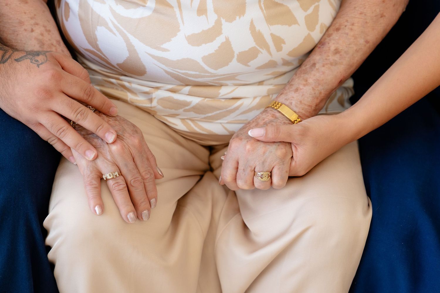Close-up of elderly and young hands holding together, wearing gold rings, symbolizing love across generations.