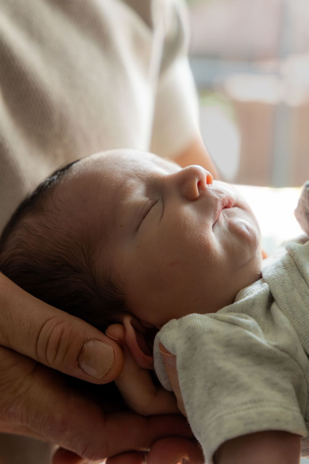 Newborn baby sleeping peacefully in parent's hands, wearing a light green onesie.
