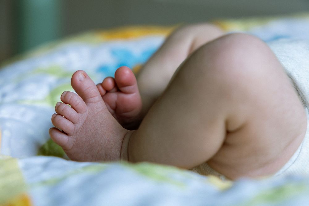 Close-up of cute baby feet and chubby legs resting on a colorful blanket.