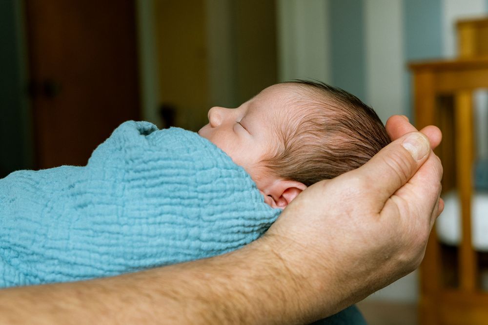 Newborn baby sleeping peacefully swaddled in a blue blanket cradled in adult hands.