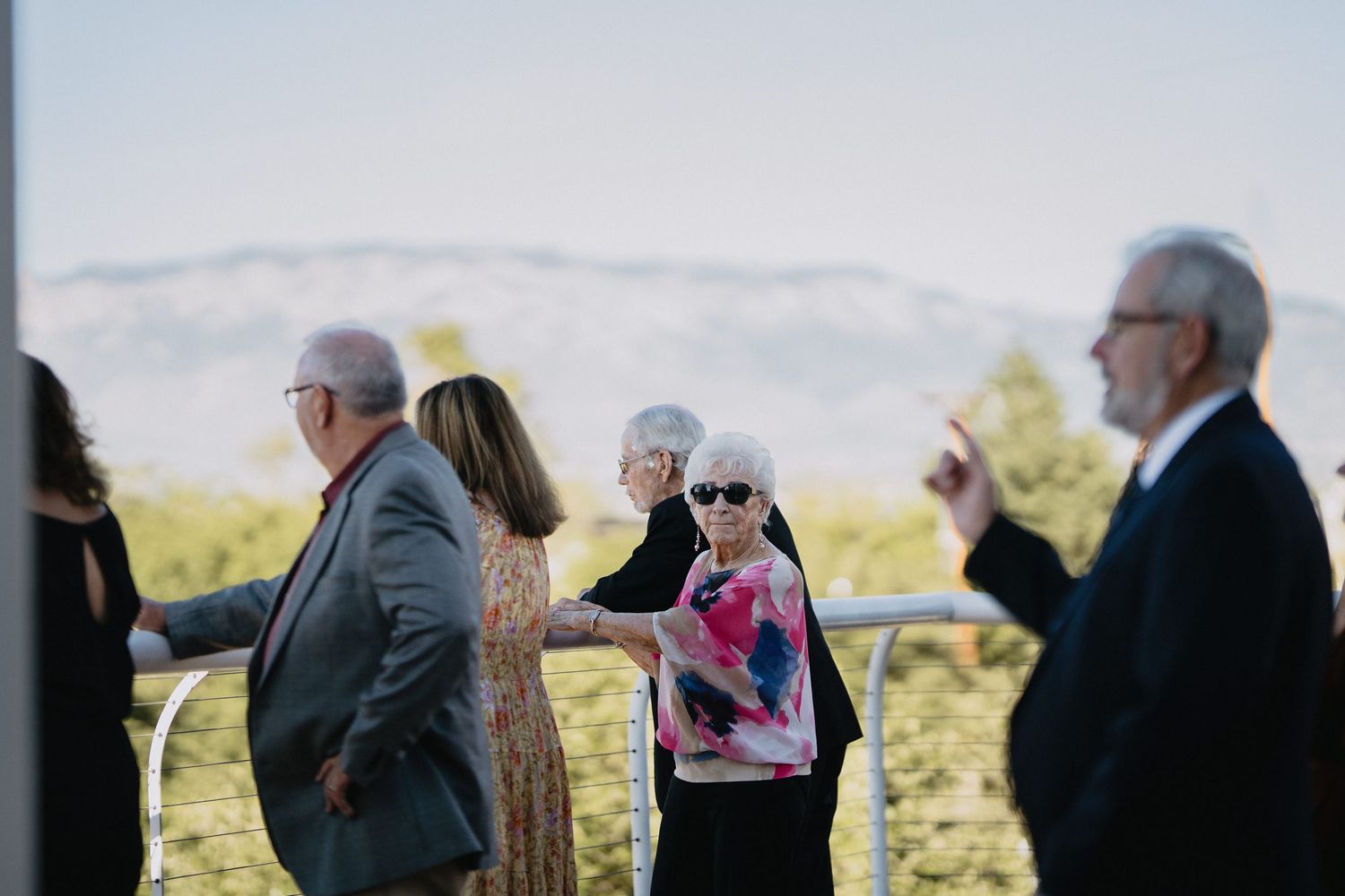 Man photographing group of five smiling people posing on outdoor terrace at a wedding celebration.