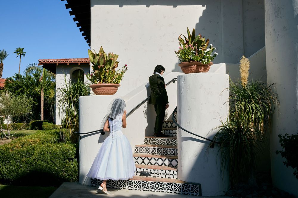 Bride and groom in white dress and black suit ascending tiled steps at a Spanish-style venue.