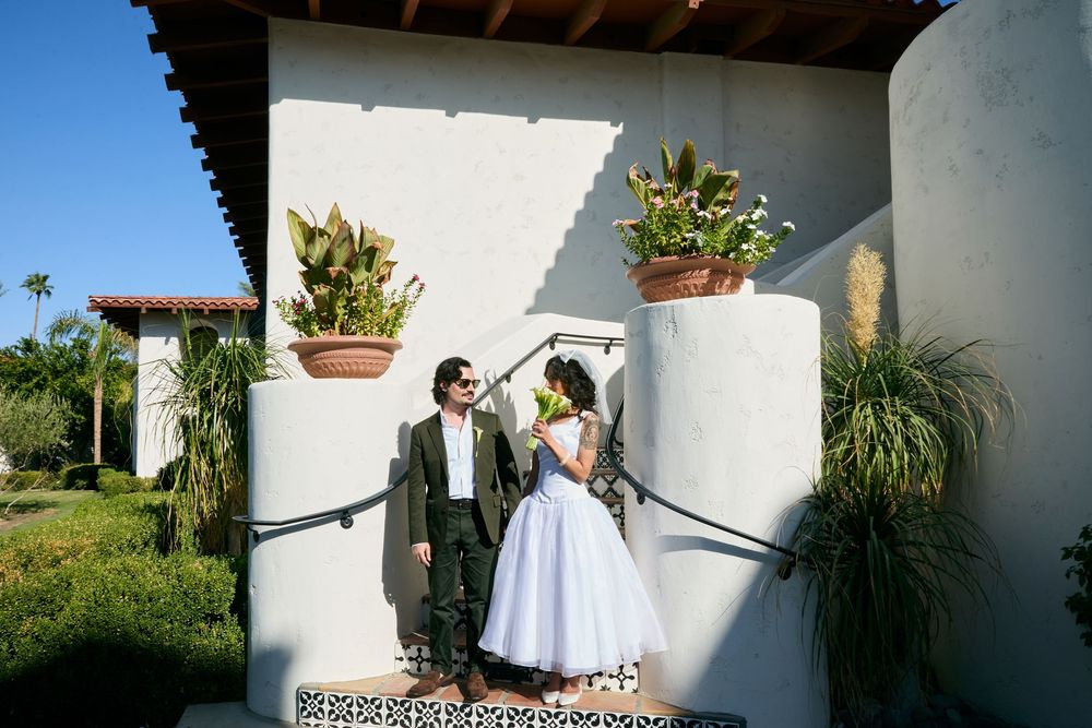 Bride and groom share romantic moment outside white stucco Spanish-style wedding venue with lush greenery.