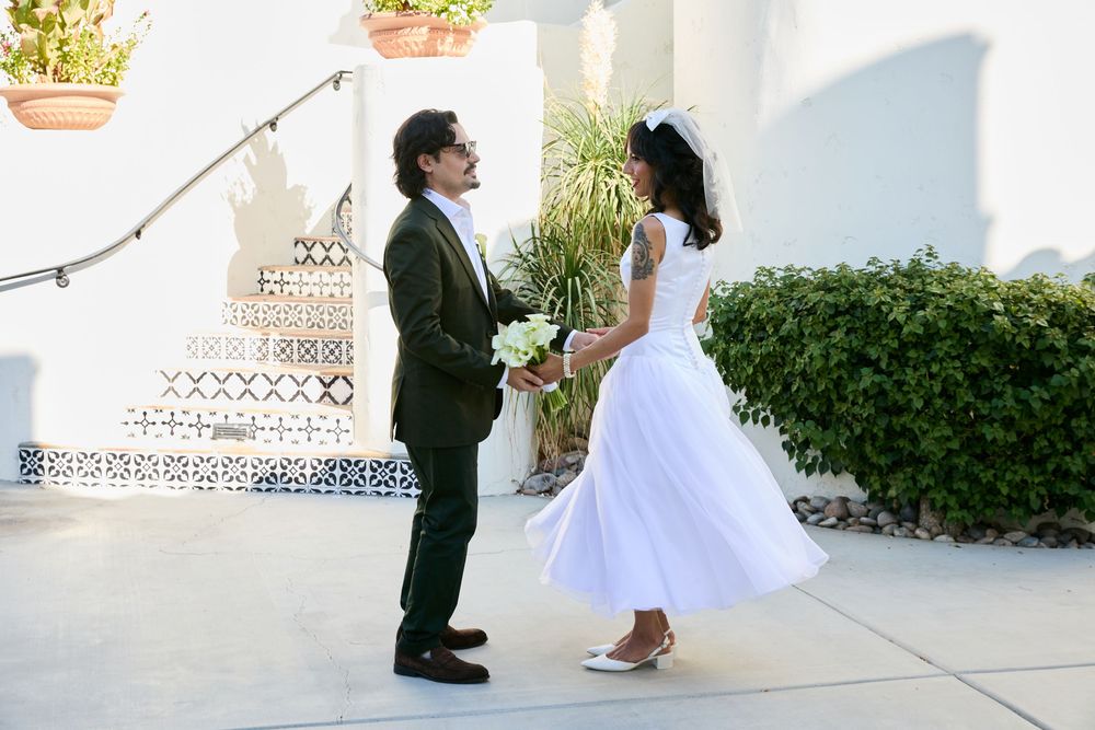 Bride and groom facing each other outdoors at a wedding venue surrounded by lush greenery.