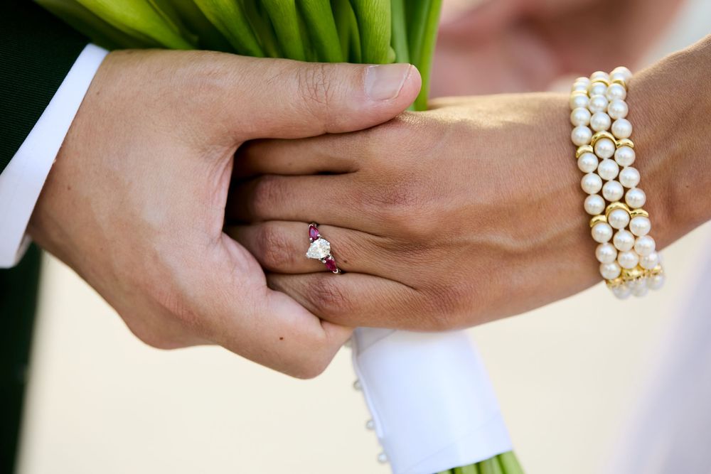 Close-up of bride's diamond engagement ring and pearl bracelet while holding a white bouquet.