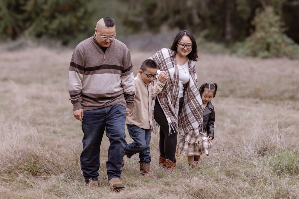 Family of four walks through a grassy meadow, wearing cozy fall outfits, with trees in the background.
