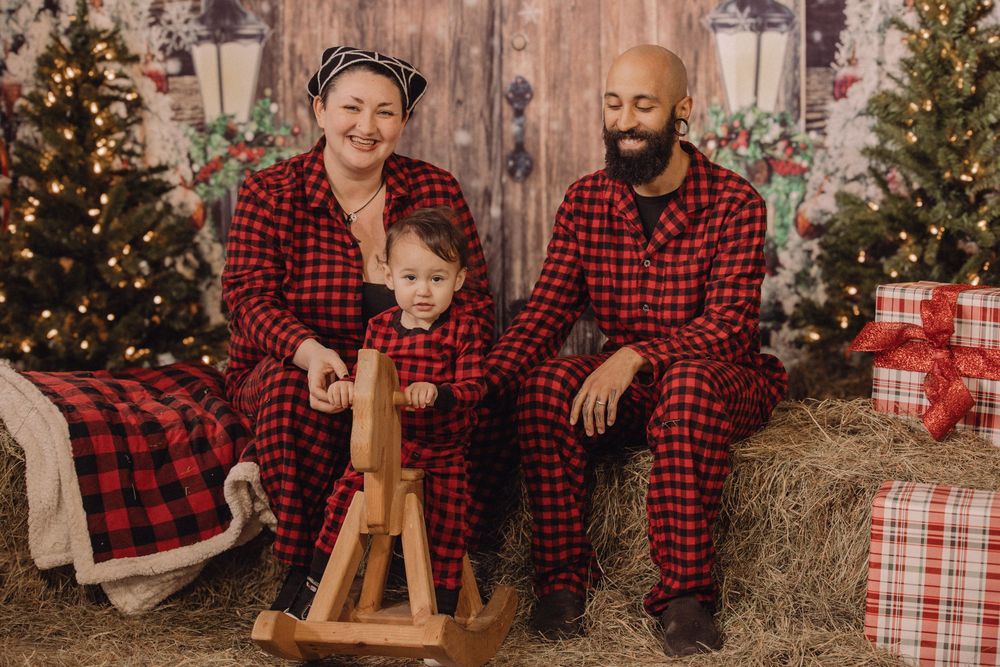 Family in matching red plaid pajamas posing with a wooden rocking horse in a festive Christmas-themed setting.