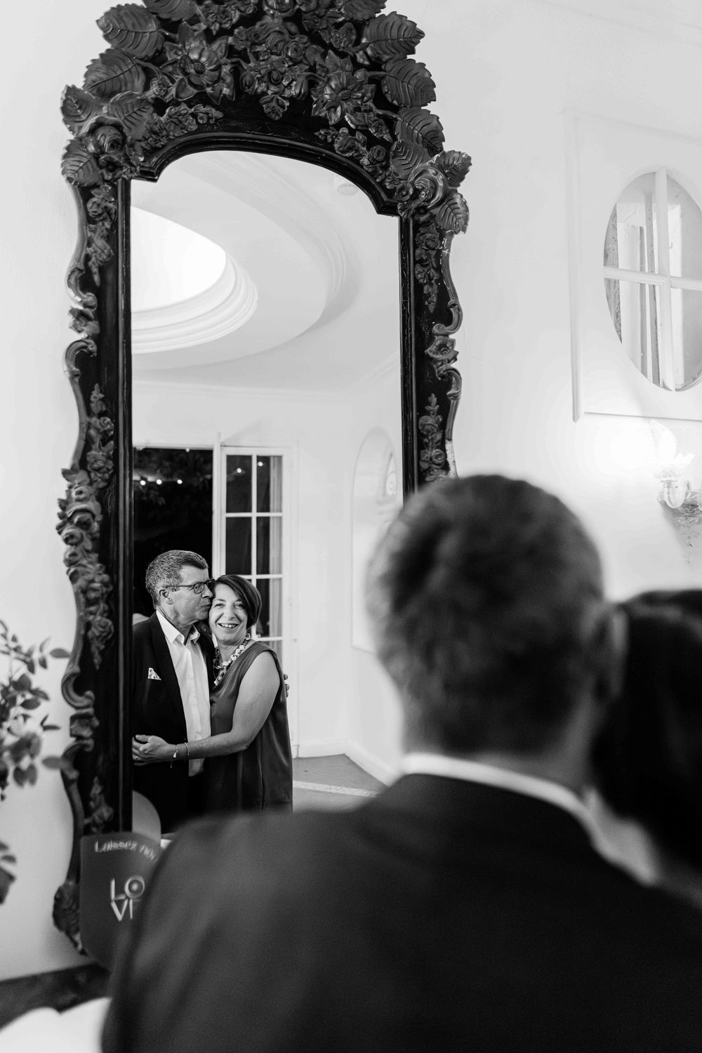 Black and white photo of a couple reflected in an ornate mirror at an elegant wedding venue.